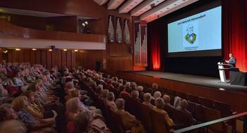 Viele Gäste sitzen in einem großen Saal und blicken auf die Leinwand, öffnet größere Ansicht