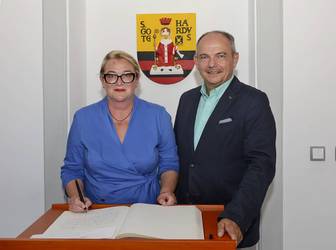 Knut Kreuch und Katrin Budde stehen vor dem Wappen der Stdat Gotha mit dem Goldenen Buch davor auf einem Tisch liegend, öffnet größere Ansicht.