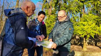 Drei Menschen betrachten eine Planzeichnung in einem Wald, öffnet größere Ansicht.