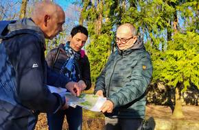 Drei Menschen betrachten eine Planzeichnung in einem Wald, öffnet größere Ansicht.