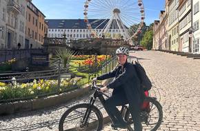 Eine Frau Ssteht mit einem Fahrrad vor einem Riesenrad, öffnet größere Ansicht