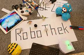 Ein Zettel mit der Schrift Robothek liegt auf einem Tisch mit kleinen MInirobotern daneben.