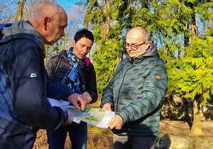 Drei Menschen betrachten eine Planzeichnung in einem Wald, öffnet größere Ansicht.