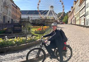 Eine Frau Ssteht mit einem Fahrrad vor einem Riesenrad, öffnet größere Ansicht