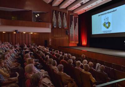 Viele Gäste sitzen in einem großen Saal und blicken auf die Leinwand, öffnet größere Ansicht