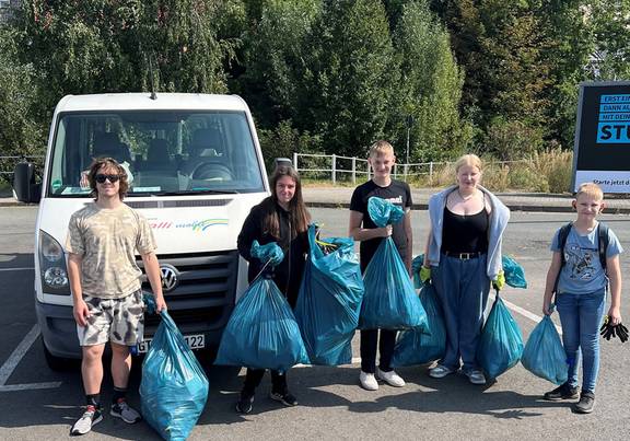 Kinder stehen mit blauen Mülltüten vor einem Kleinbus, öffnet größerer Ansicht.